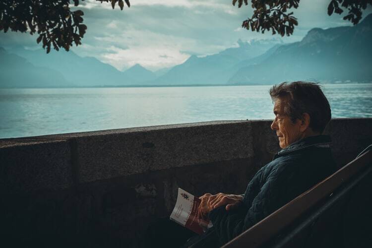 An older wise man reading a book by the water 