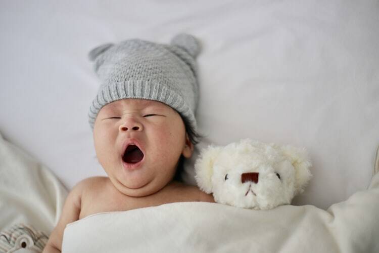 A healthy baby yawning next to a teddy bear