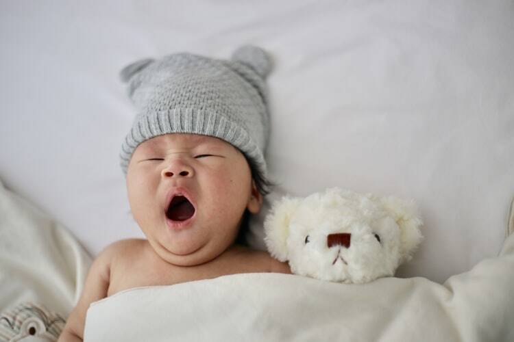 A healthy baby yawning next to a teddy bear 