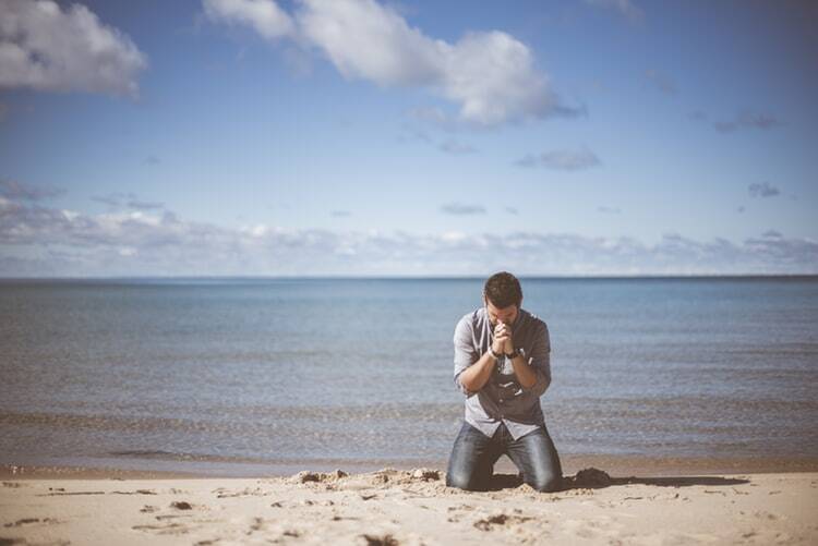 A man with his hands folded practicing gratitude on a beach
