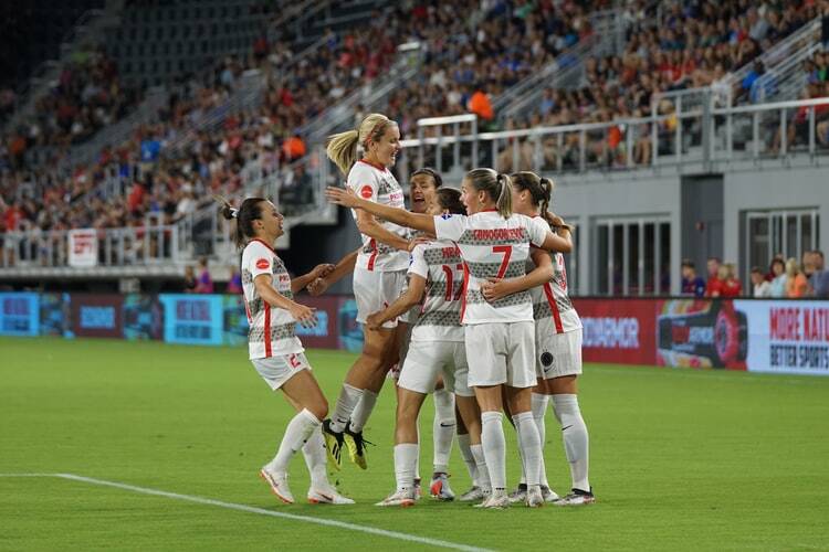 A women's soccer team celebrating a goal as the crowd goes wild.